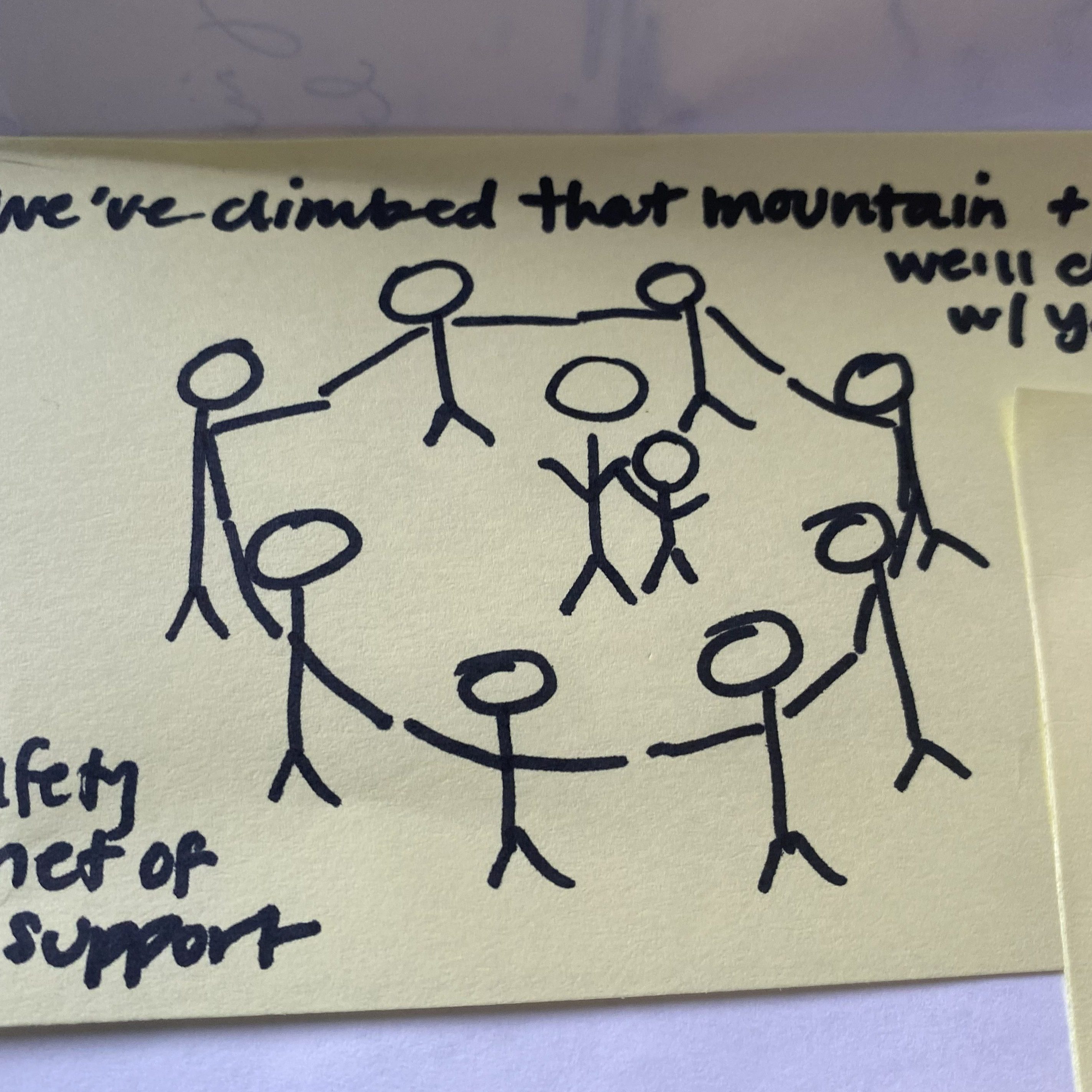 A sticky note with a drawing of stick-figure people holding hands in a circle with the hand-written text: "We've climbed that mountain and we'll climb it with you. Safety net of support."